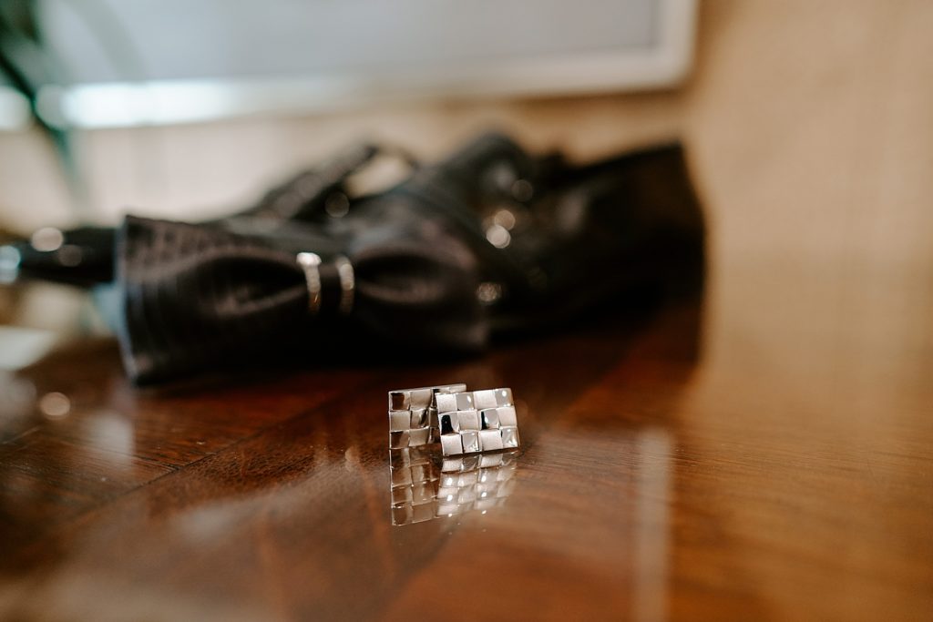 Detail shot of cuff links in front of bowtie and shoes