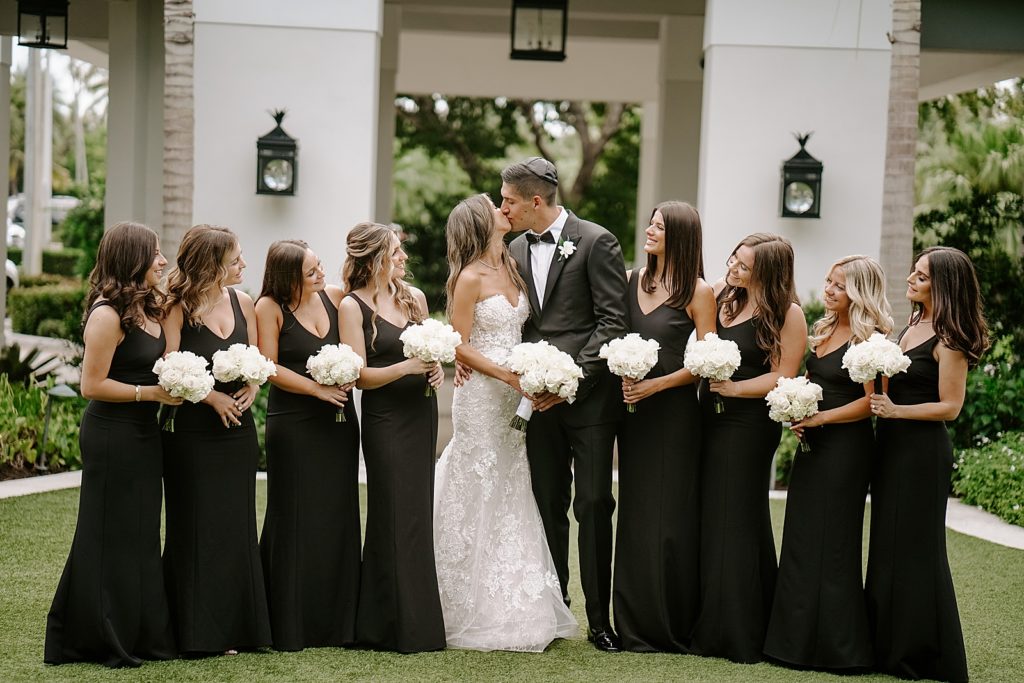 Bride and Groom kissing with Bridesmaids watching holding white bouquets